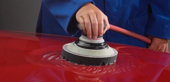 Un travailleur d’atelier de carrosserie qui prépare le capot d’une voiture rouge pour la peinture.
