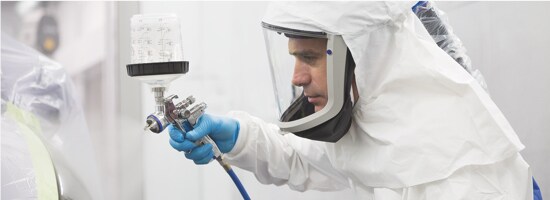 A worker wearing a full protective suit, face mask, and gloves, operating a 3M™ PPS™ 2.0 system.
