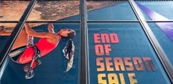 Windows of a building with graphic films depicting a rock climber and advertising an end of season sale.
