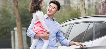 Homme debout à côté d’une voiture, tenant sa fille dans ses bras.
