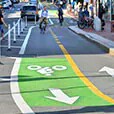 Biker on a dedicated bike lane painted green in a busy urban city marked with a sharrow.