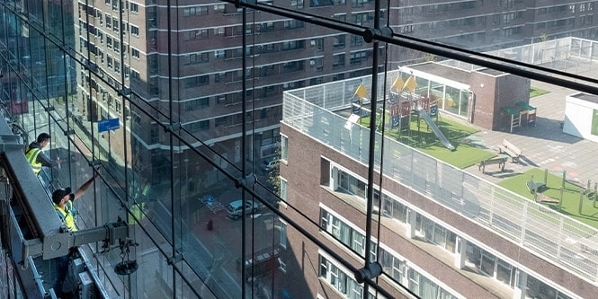 Des ouvriers sur un échafaudage appliquent une pellicule pour fenêtres sur une façade en verre.
