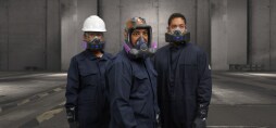 Trois travailleurs se tiennent debout dans un environnement industriel, tous portant une combinaison de protection bleu foncé.
