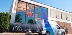 A van parked in front of a building that has graphic films on its windows depicting a rock climber.
