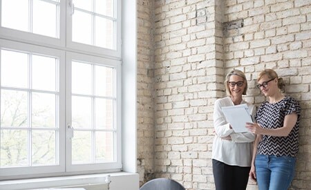 Deux personnes se tiennent près d’une fenêtre, baignant dans la lumière qui éclaire leur environnement.
