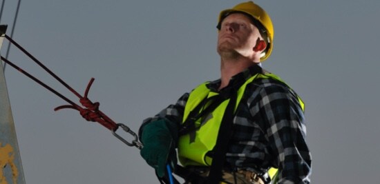 Un électricien portant un casque de protection, attaché avec du matériel de protection contre les chutes.
