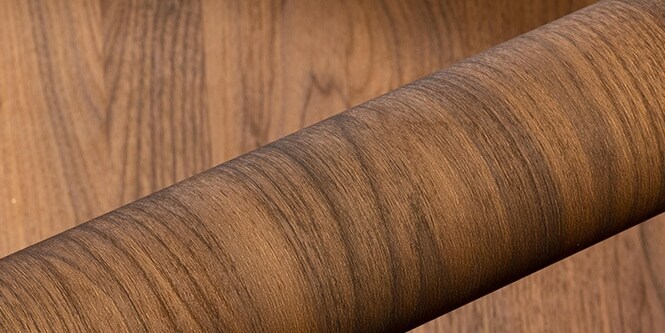 Un rouleau de finition architecturale DI-NOC effet bois sur fond de bois.
