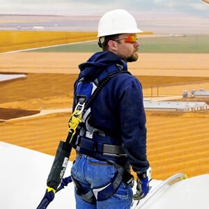 Travailleur avec harnais et casque de sécurité sur une structure élevée.