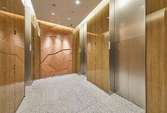 Baie d’ascenseur habillée d’une finition pour verre DI-NOC 3M à l’aspect bois, conférant élégance et chaleur aux murs.
