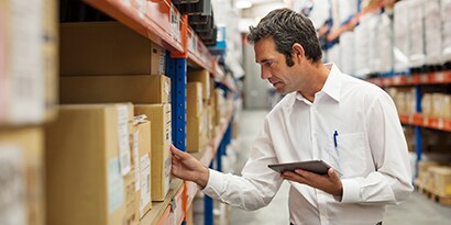 Man in a warehouse holding a tablet reviewing a label on a box.
