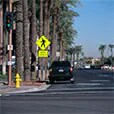 Highly flourescent and visible pedestrian cross walk sign viewed from a distance with a car approaching.