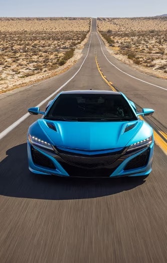 A bright blue sports car drives down an empty desert highway, showcasing its sleek design and vibrant colour.
