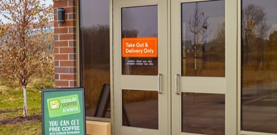 Les portes d’entrée d’un magasin et une pancarte sur la porte indiquant que seuls les plats à emporter et la livraison sont autorisés.
