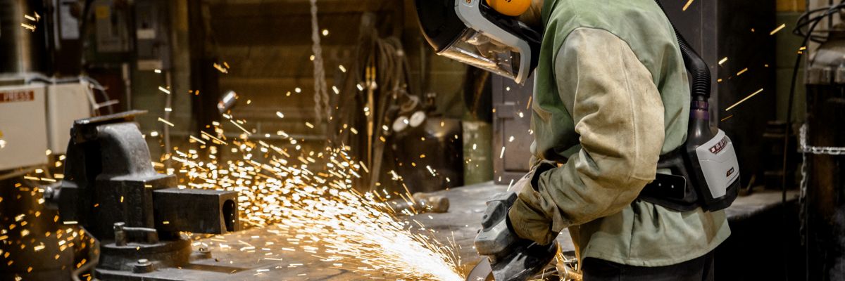 A metalworker wearing a variety of 3M personal protective equipment, grinding a piece of metal with 3M power tools.
