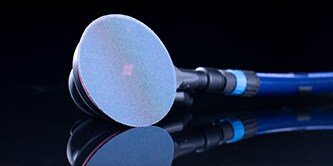 Close-up of a handheld power sander with a blue abrasive disc, shown against a dark reflective surface.
