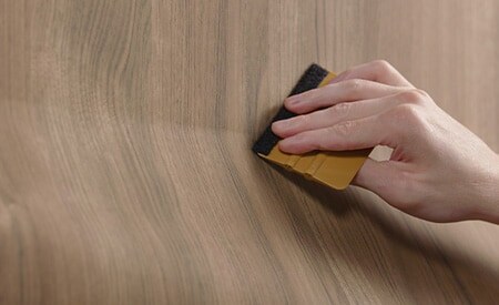 Gros plan sur un outil de raclage appliqué à l’installation d’une pellicule à effet bois.
