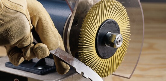 A worker preparing to use a 3M™ Scotch-Brite™ Radial Bristle Brush to polish a piece of metal.
