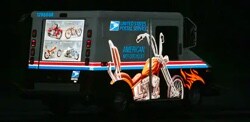 A postal service van wrapped in reflective film at night.
