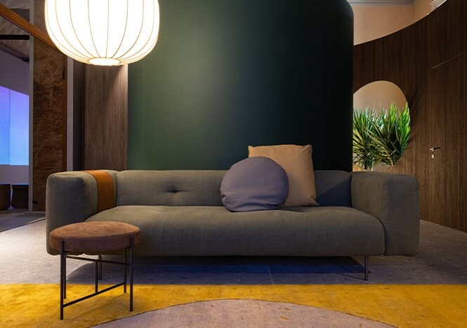 Round room featuring dark wood finish wall and matte green column with gray couch centered in frame.