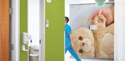 The wall of a hospital hallway with a graphic film on a wall of a baby hand holding a teddy bear.
