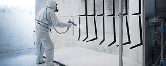 Image of a worker in protective gear applying powder coat paint to metal parts.
