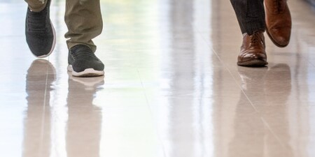 Vue recadrée à partir des genoux de deux personnes qui marchent sur un plancher de bâtiment commercial nouvellement poli.
