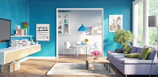 Un salon équipé d’une télévision fixée à un mur, en face d’un canapé placé devant une fenêtre.
