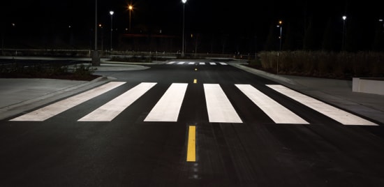 Highly visible pavement markings, including crosswalk and lane dividing line, at night.
