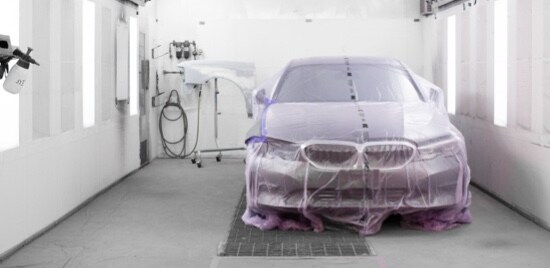 Une voiture dans une cabine de peinture recouverte de ruban de masquage et d’une pellicule.
