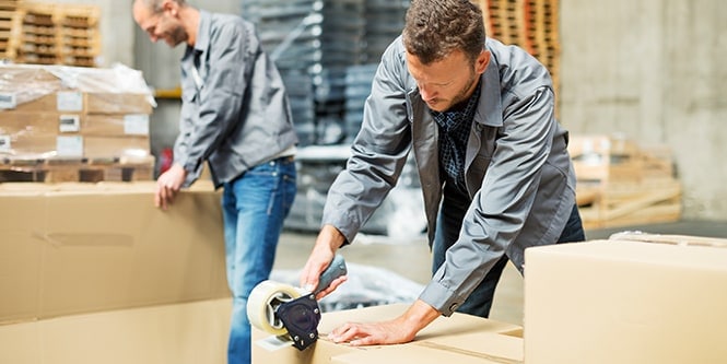 Deux ouvriers scellent des cartons d’expédition dans un entrepôt.
