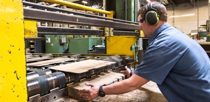 Un travailleur avec appareil auditif utilise des machines au travail. La machine est équipée de protections de sécurité jaunes et des tôles y sont traitées. 
