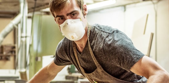 Un homme portant un respirateur jetable, qui fait des travaux de construction dans son garage.