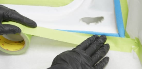 Un travailleur qui applique du ruban de masquage sur une voiture.
