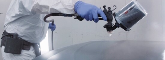 Un peintre en combinaison pulvérisant de la peinture noire sur une voiture à l’aide d’un Pistolet de pulvérisation à haute performance 3M(MC).
