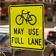 Bright yellow reflective sign indicating bikes have full lane use.