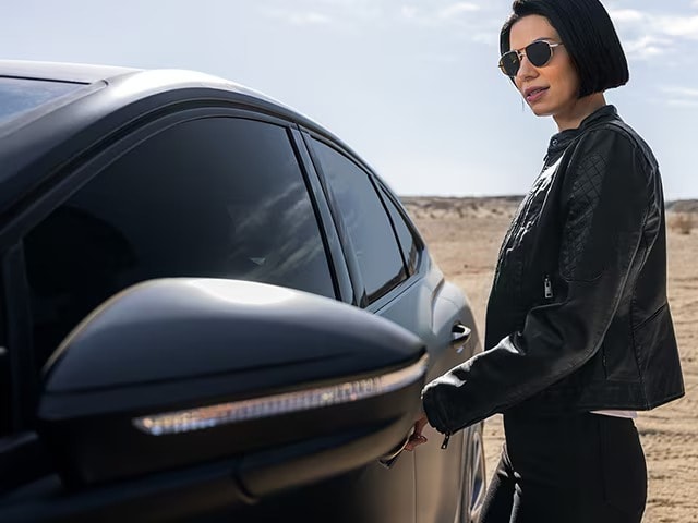 Woman grabbing door handle of black sedan with matte paint protection film in the desert.
