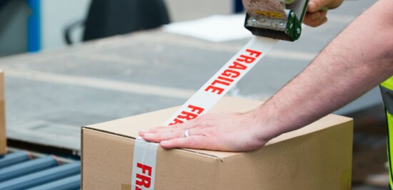 A person sealing a box with tape that has the word 'fragile' on it.
