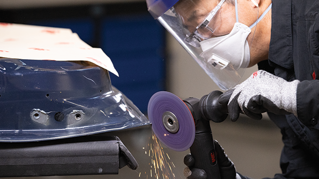 Technicien utilisant un disque abrasif 3M sur une surface métallique tout en portant un équipement de protection.
