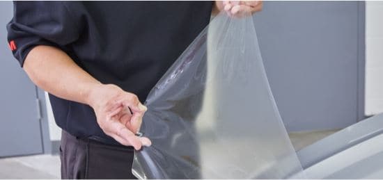 A professional installer applying paint protection film to a car.
