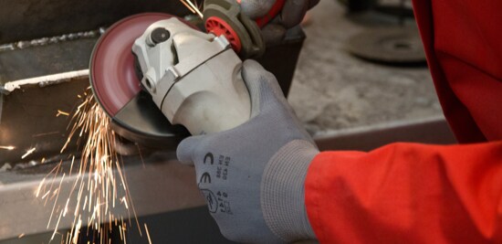 A metalworkers gloved hands, using a powertool to grind a piece of metal.
