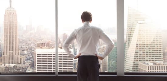 Un homme regarde par une fenêtre donnant sur la ligne d'horizon de la ville.
