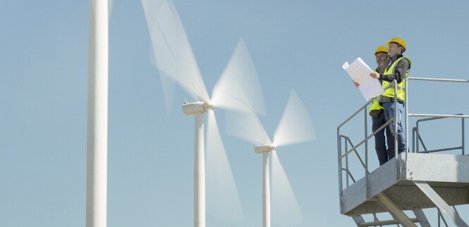 Two workers in front of three wind turbines.
