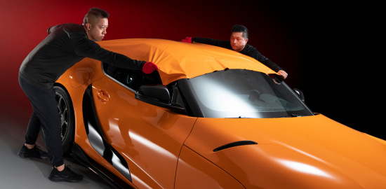 Des techniciens automobiles installent une pellicule de protection pour la peinture sur le toit d’une voiture de sport.
