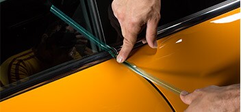 A person applying 3M™ Bridge Line Knifeless Tape to the gap on one side of a car door.
