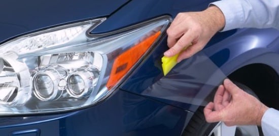 A worker applying paint protection film to the fender of a car.
