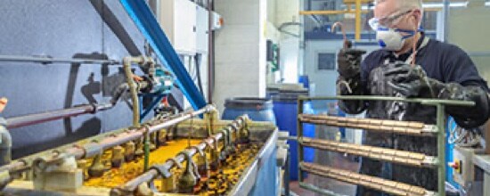 Image of a worker in protective gear preparing to hang a rack of parts in an electroplating bath.
