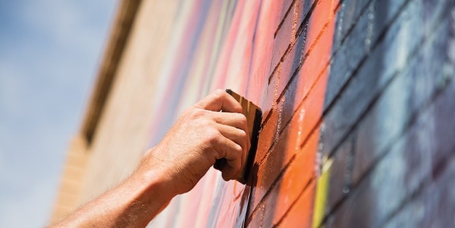 Gros plan sur une main manipulant un outil pour poser une pellicule pour graphismes imprimée sur un mur de briques.
