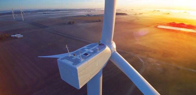 Une imposante éolienne se dresse sur une vaste plaine au lever ou au coucher du soleil.
