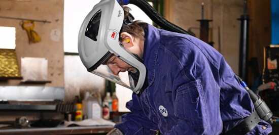 Les mains gantées d’un métallurgiste utilisant un outil électrique pour meuler une pièce de métal.
