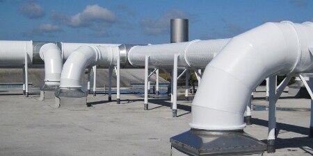 A series of large white industrial ventilation ducts on a rooftop, designed for air circulation and exhaust, set against a clear blue sky.
